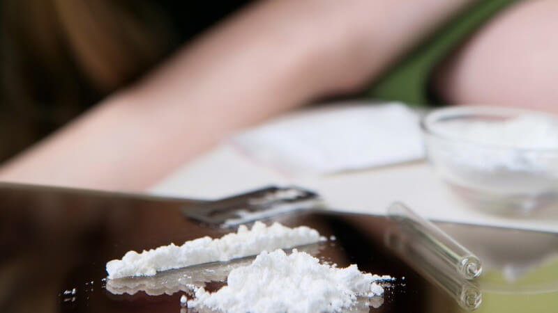 Drogen in Pulverform auf Glasplatte, im Hintergrund junge Frau