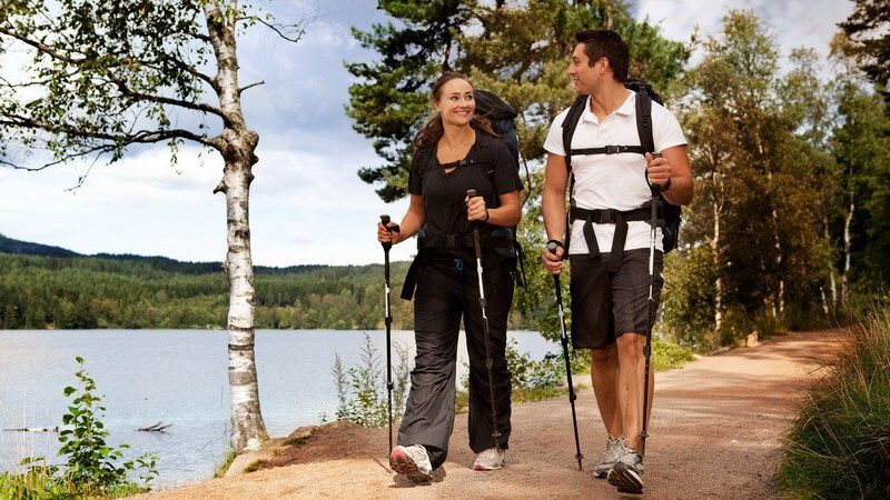 Backpacking, junges Paar beim Wandern mit Stöcken und Rucksack am See