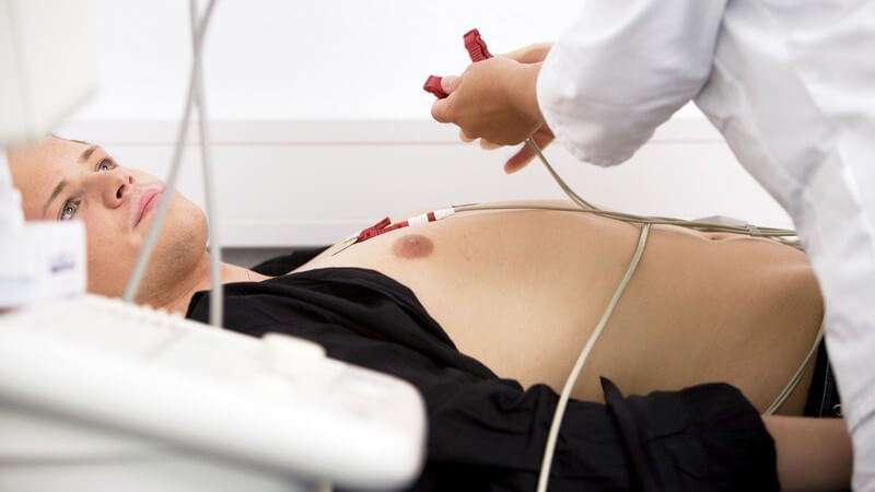 Arzt bringt EKG Elektroden auf Brust eines Patienten an