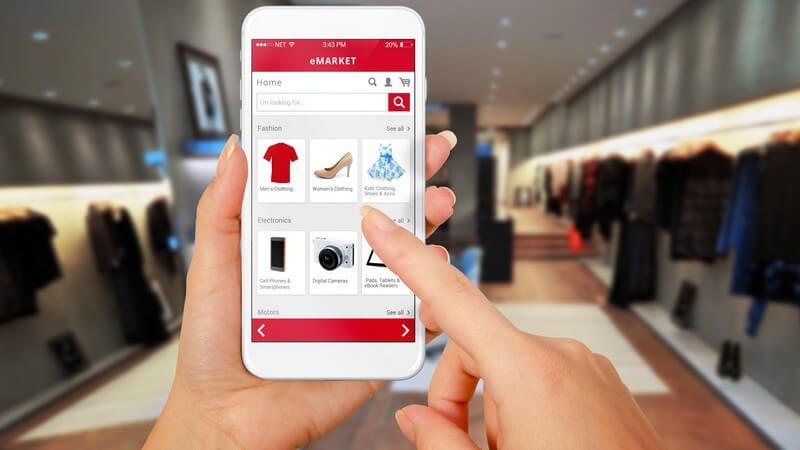 Frauenhände halten ein Smartphone, Shopping von Mode in einem Onlineshop, im Hintergrund ein Modegeschäft