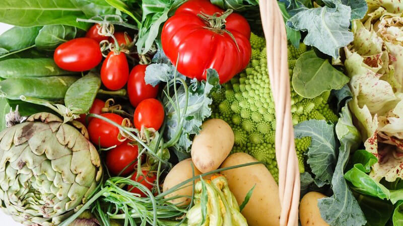Großer Weidenkorb voll mit frischem Gemüse wie Tomaten, Romanesco, Artischocke und Kartoffeln