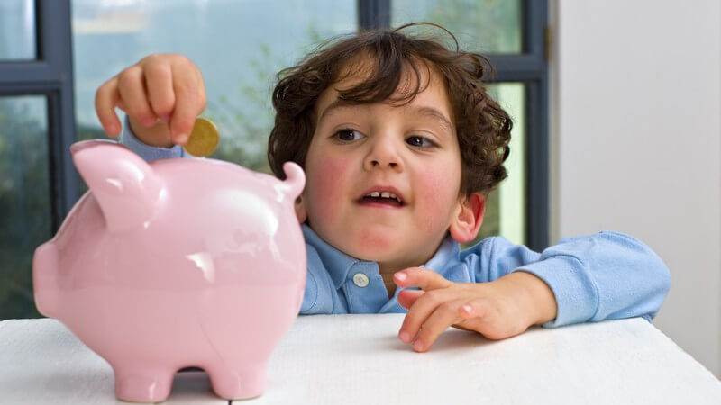 Kleiner Junge wirft Münze in rosanes Sparschwein