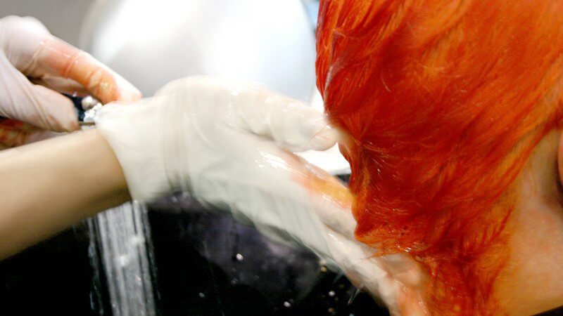 Nahaufnahme Hände mit Gummihandschuhen waschen rotgefärbte Haare