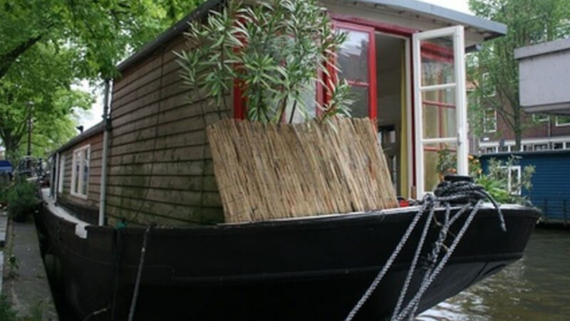 Hausboot aus Holz, umgeben von grünen Pflanzen auf einem Fluss