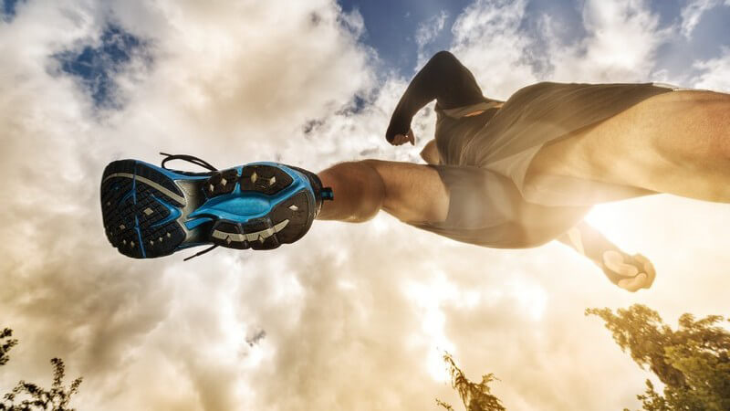 Jogger mit blauen Laufschuhen aus der Bodenperspektive mit dem Himmel als Hintergrund