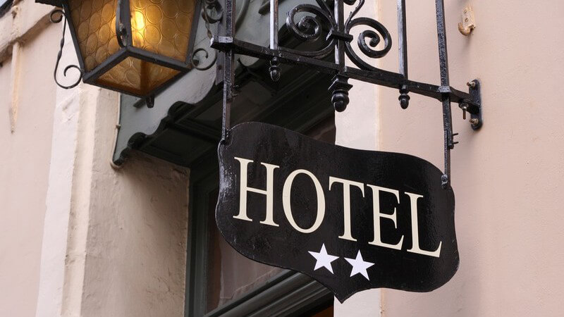 Schild an der Seite eines Hauses mit Laterne, Aufschrift "HOTEL" und zwei Sterne