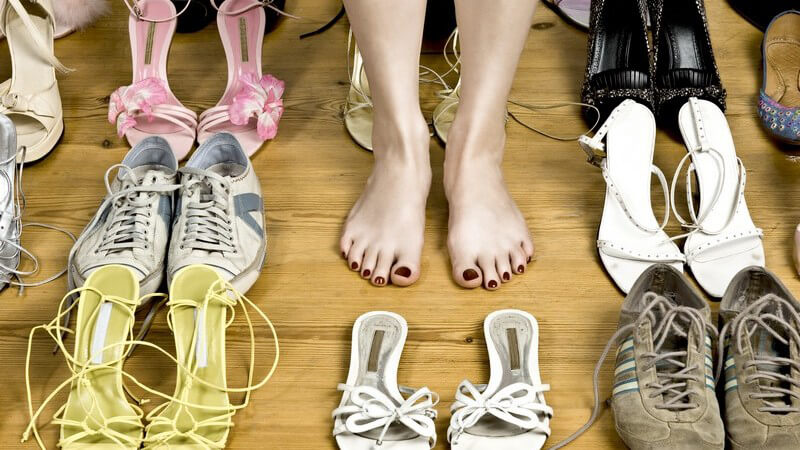 Nackte Frauenfüße auf Holzboden zwischen vielen Schuh-Paaren