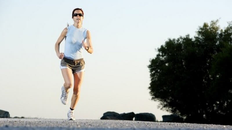 Sportliche Frau mit Sonnenbrille, die Straße hoch joggend