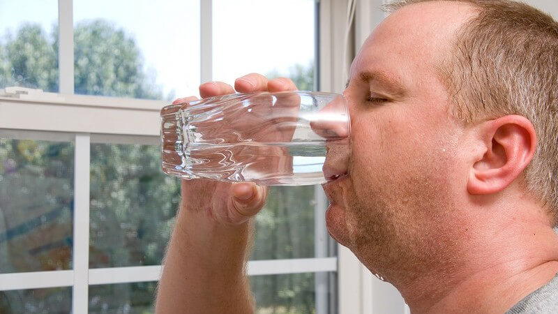 Mann trinkt aus Glas, Wasser läuft ihm das Kinn hinunter