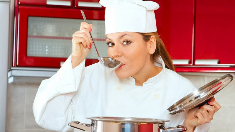 Junge Köchin an Kochtopf probiert Essen mit Suppenkelle