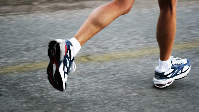 Beine einer Läuferin mit Laufschuhen auf grauem Asphalt