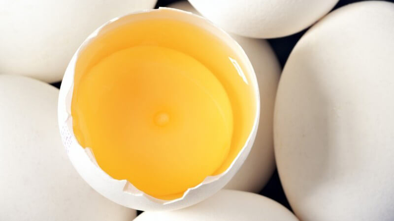Weiße Eier, eins aufgeschlagen, Eigelb