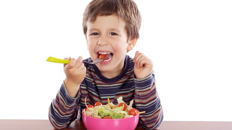 Kleiner Junge sitzt am Tisch und isst frischen Salat