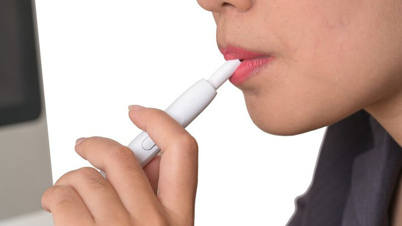 Frau mit rotem Lippenstift raucht eine weiße Hybrid-Zigarette