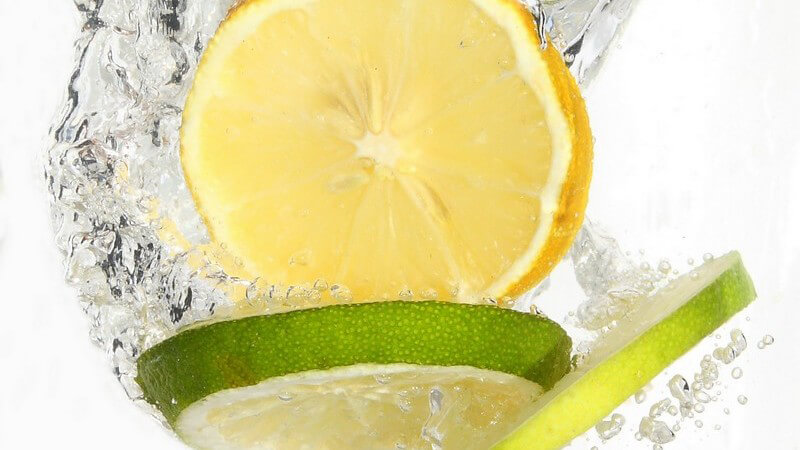 Zitronen- und Limettenscheiben fallen ins Wasser