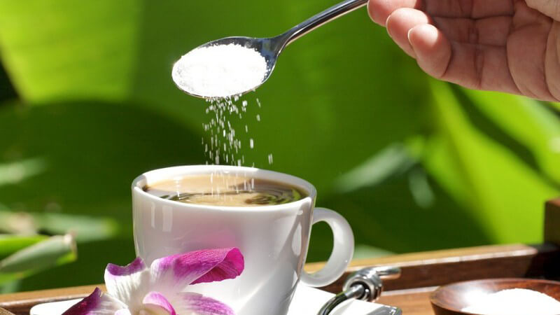 Nahaufnahme Löffel Zucker wird in Tasse Kaffee gekippt