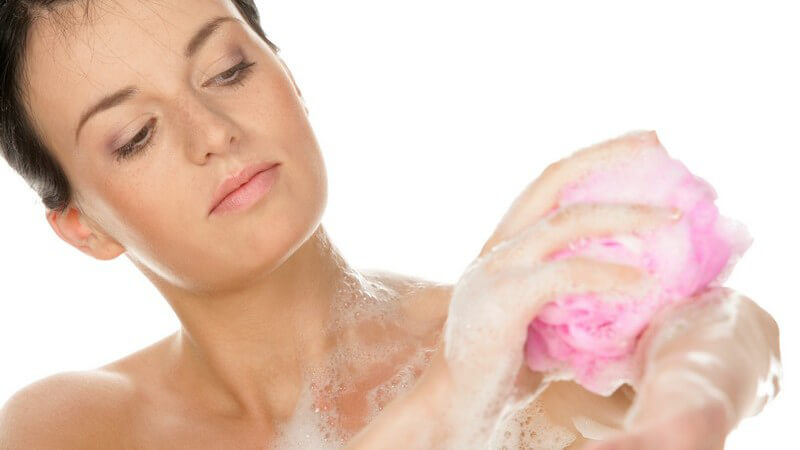 Junge Frau wäscht sich mit Schwamm, weißer Hintergrund