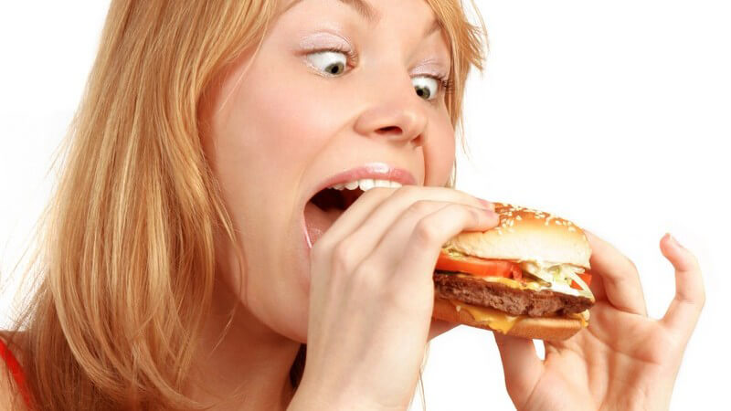 Hungrige Frau beißt mit aufgerissenen Augen in einen Burger