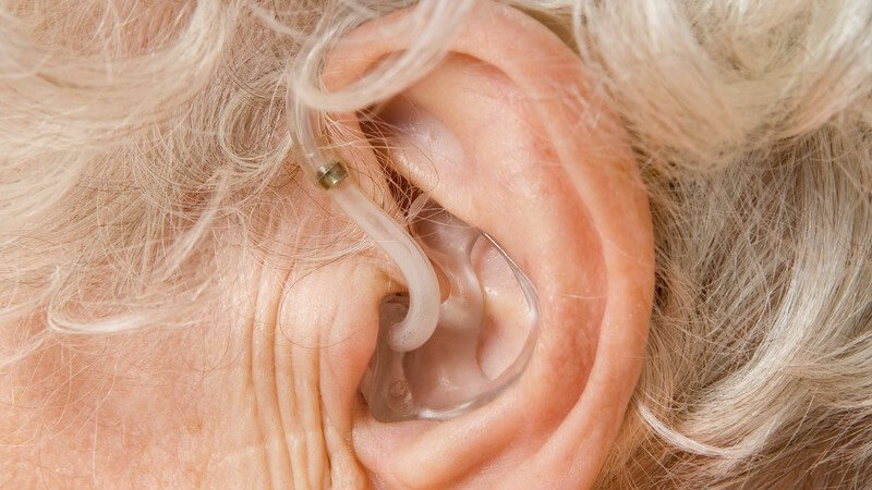 Linkes Ohr mit Hörgerät einer alten Frau mit grauen Locken