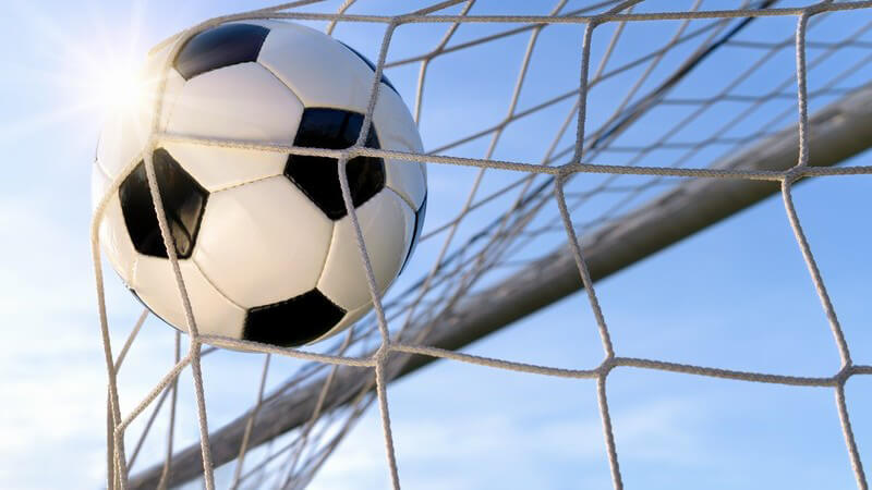 Fußball im Netz des Fußballtors unter blauem Himmel