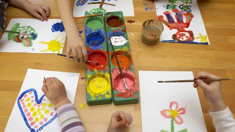 Gruppe von Kindern sitzt am Tisch und malt mit Wasserfarben