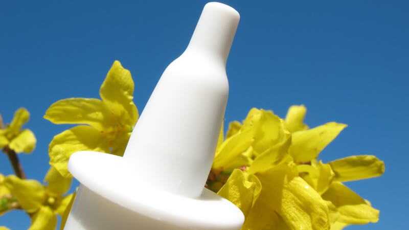 Nahaufnahme Nasenspray-Düse gelbe Blumen, Pollen, Pollenallergie, vor blauem Himmel