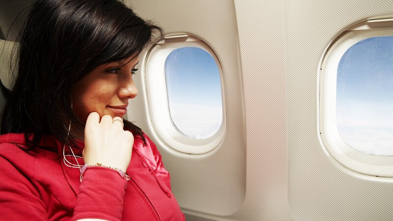 Junge Frau sitzt lächelnd im Flugzeug am Fensterplatz