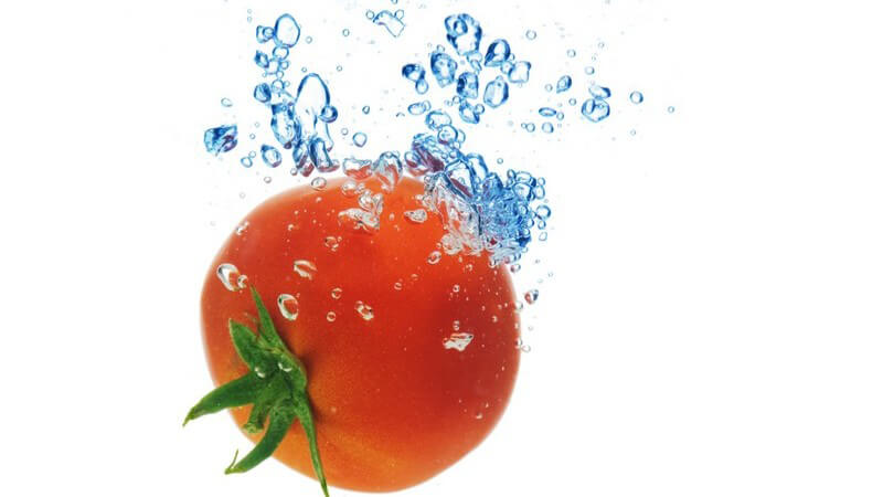 Tomate fällt ins Wasser und hinterlässt Wasserblasen unter Oberfläche