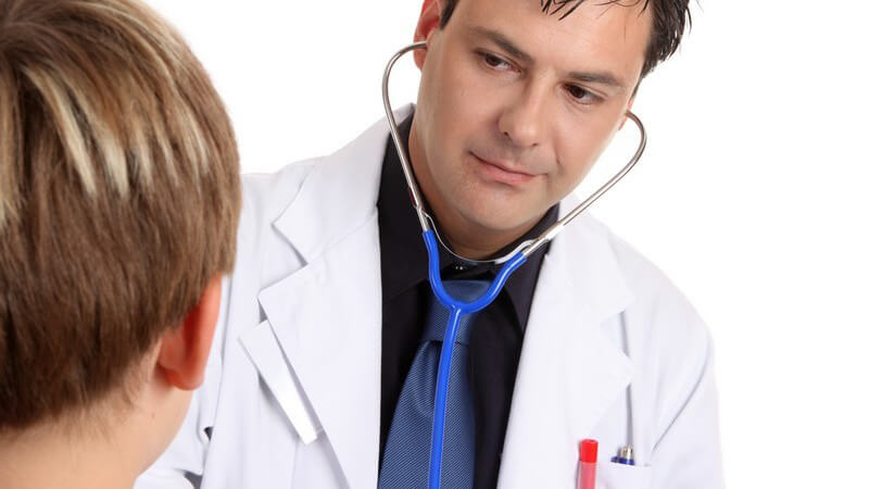 Arzt mit weißem Kittel und blauem Stethoskop im Ohr untersucht einen Jungen
