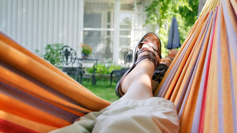 Hängematte in Garten, Blick auf eigene Füße mit Sandalen und auf Gartenhaus, Natur, schönes Wetter, Bäume, Relaxen, Öko