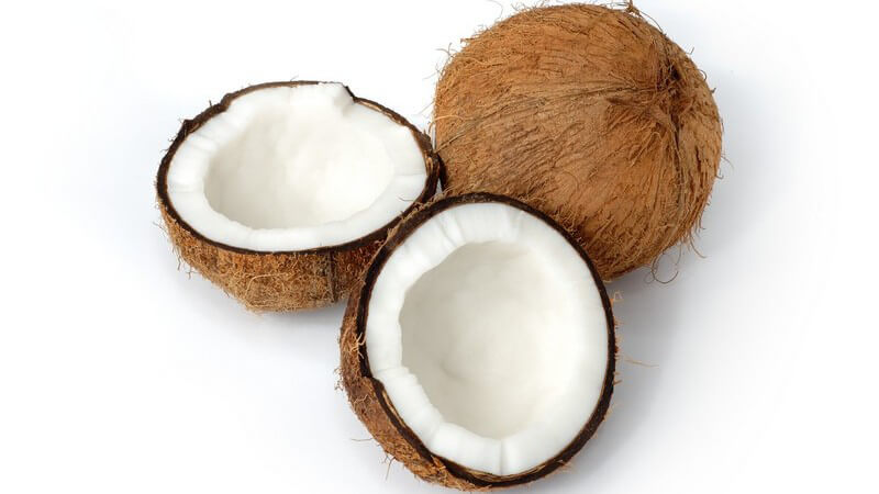 Zwei Kokosnüsse, eine halbiert, auf weißem Hintergrund