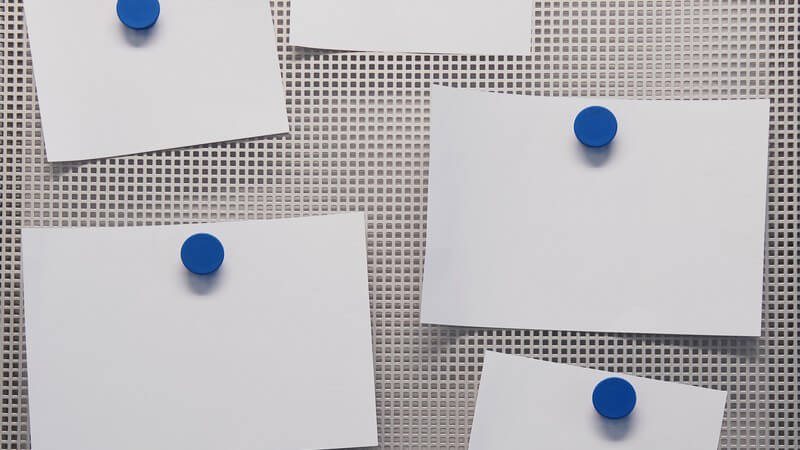 Weiße Zettel mit blauen Magneten an Magnet-Pinnwand