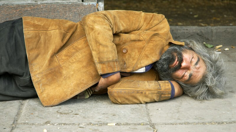 Älterer Obdachloser liegt auf Bürgersteig und schläft