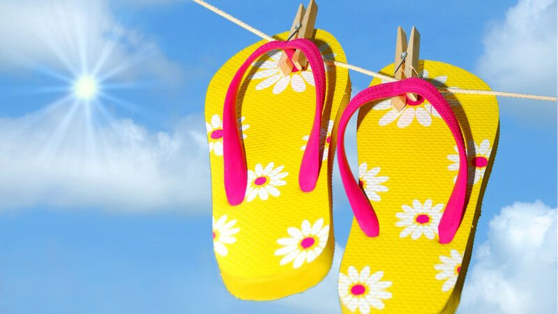 Flip-Flops hängen mit Wäscheklammern an Wäscheleine unter blauem Himmel