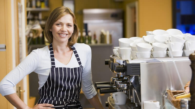 Junge, lächelnde Frau im Restaurant hinter einer Kaffeemaschine