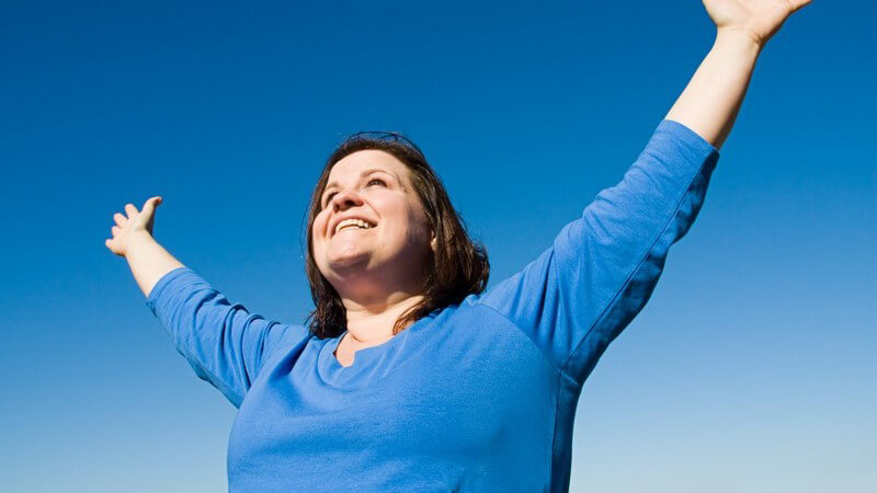 Übergewichtige Frau streckt lächelnd beide Arme in den Himmel