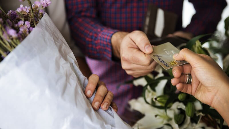 Kunde in einem Blumenladen bezahlt einen Bund lila Blumen mit der Kreditkarte