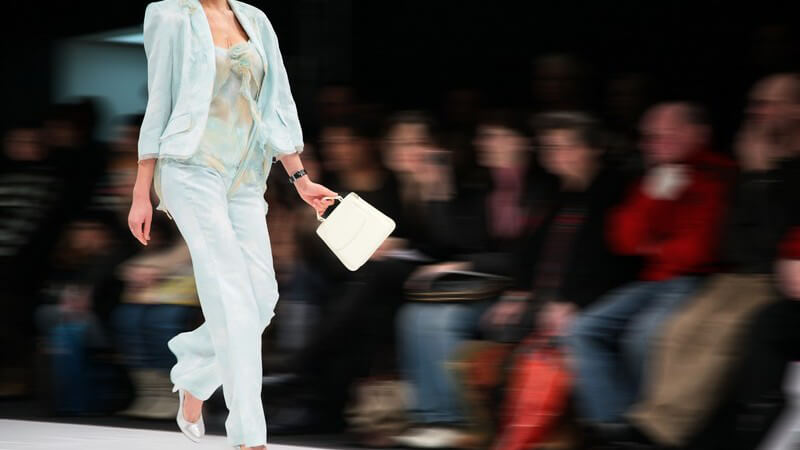 Model in weißem Hosenanzug und Handtasche läuft über den Laufsteg