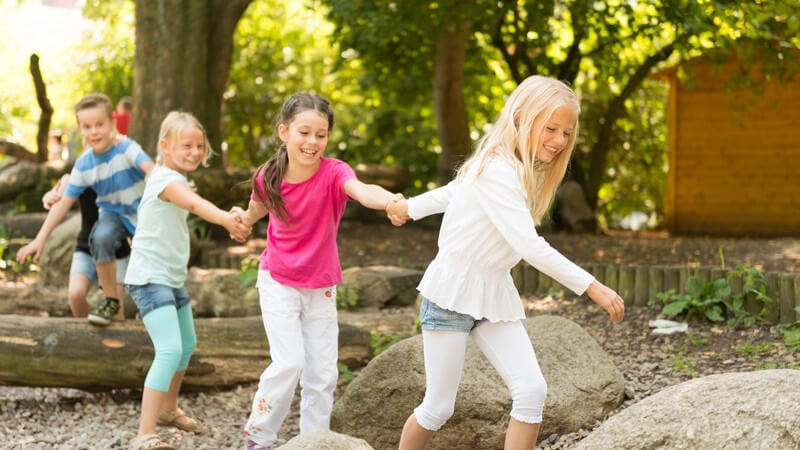 Kinder bilden händchenhaltend eine Menschenkette und klettern über Baumstämme und Steine