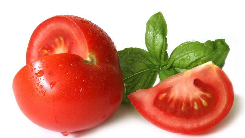 Frische Tomate, Stück ausgeschnitten, daneben frischer Basilikum