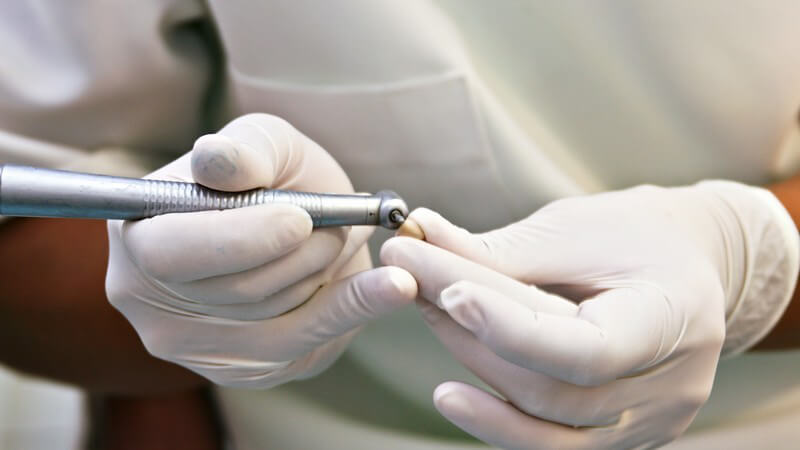 Zahnarzt mit weißen Handschuhen arbeitet mit dem Bohrer an einem losen Zahn