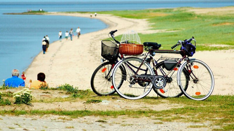 Zwei Fahrräder auf Sanddünen, dahinter Menschen am Strand