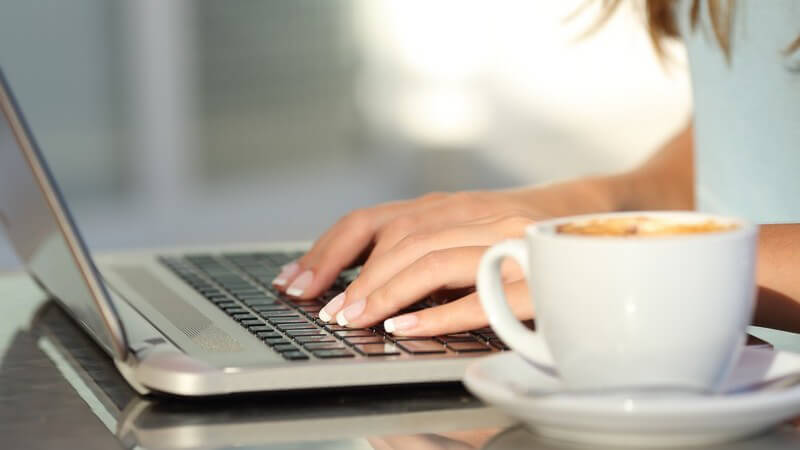 Frau tippt auf einem Laptop, daneben eine Kaffeetasse
