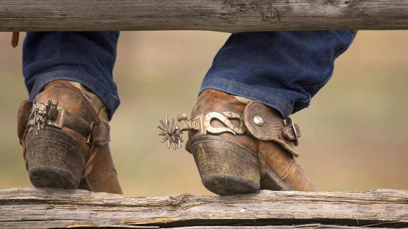 Cowboystiefel an Holzbalken gelehnt, Mann sitzt auf Holzzaun