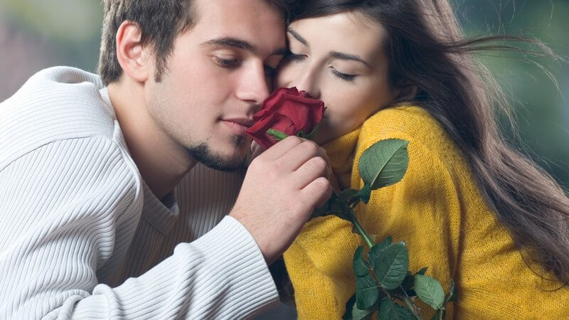 Junges Paar draußen riecht zusammen an roter Rose
