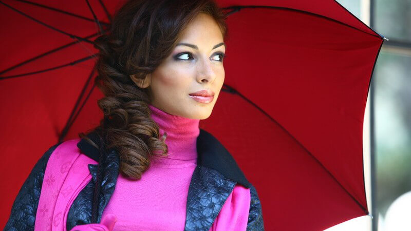 Dunkelhaarige Frau unter rotem Regenschirm
