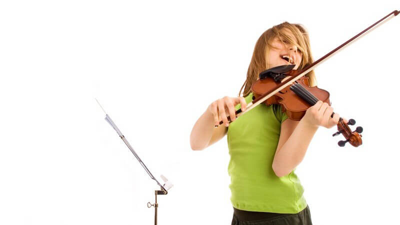 Junges Mädchen steht vor Notenständer und spielt energisch auf der Geige