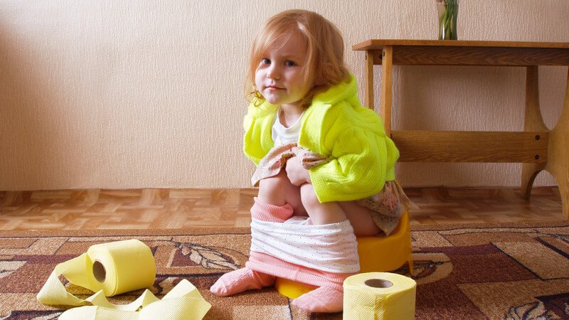Kleines Mädchen sitzt auf dem Töpfchen, neben ihr zwei Rollen Toilettenpapier