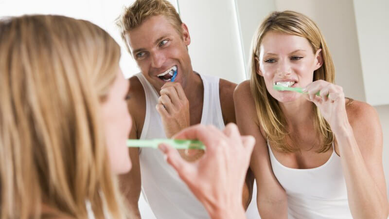 Junges Paar im Bad steht vor Spiegel und putzt Zähne