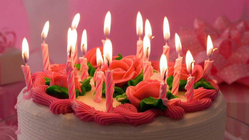 Weiß-rosa Geburtstagstorte mit Rosen und vielen Kerzen